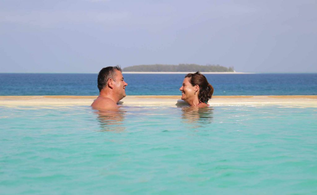Ein Paar im Infinity Pool mit der Insel Mnemba im HIntergrund
